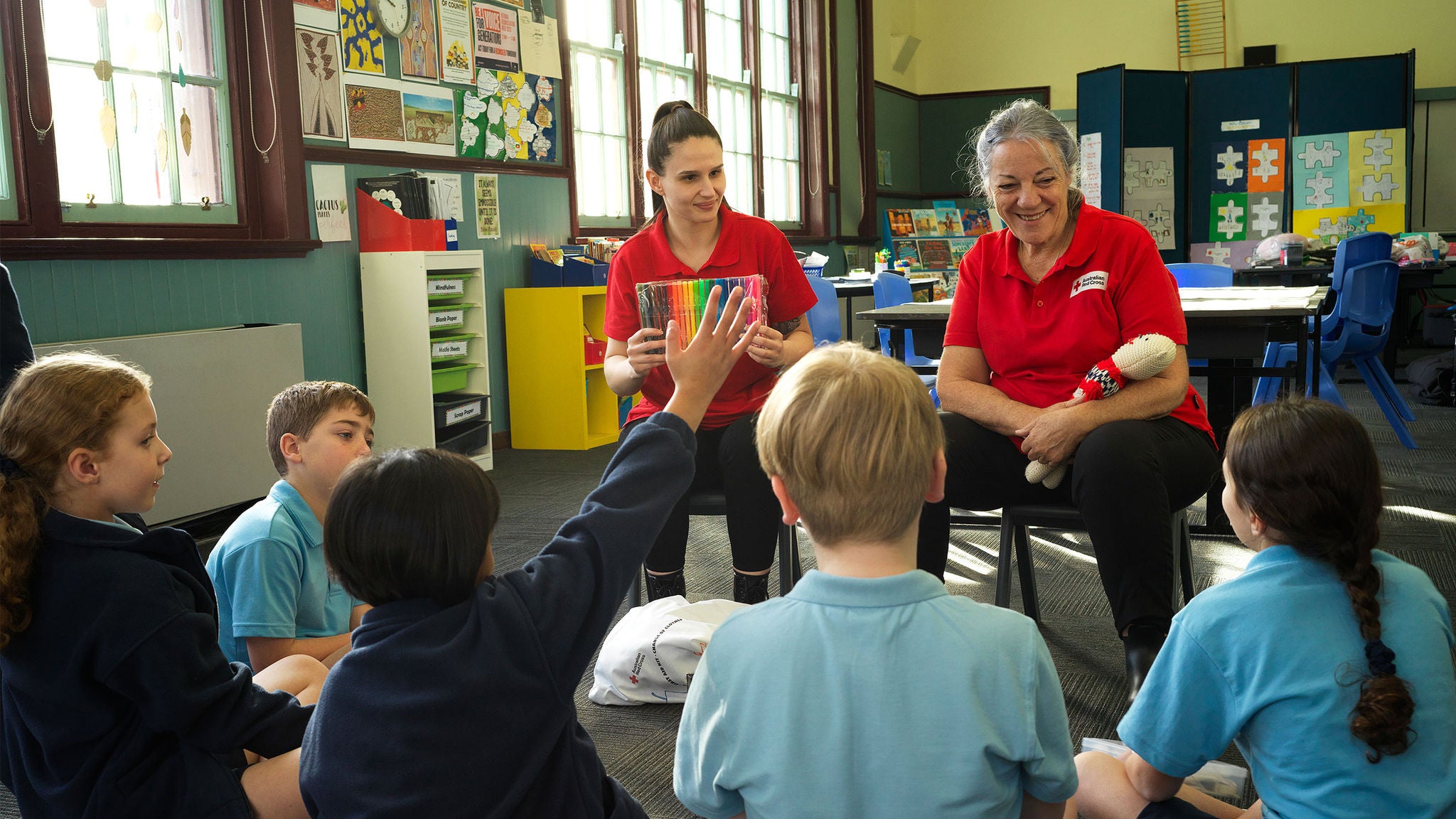 photo-two-women-red-cross-shirts-giving-talk-primary-school-children