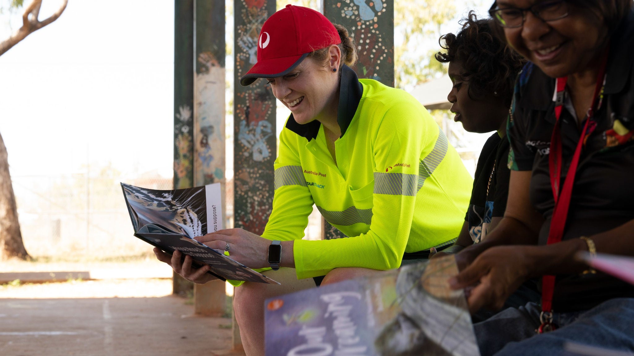 photo-female-postie-reading-a-book-sitting-with-indigenous-kids