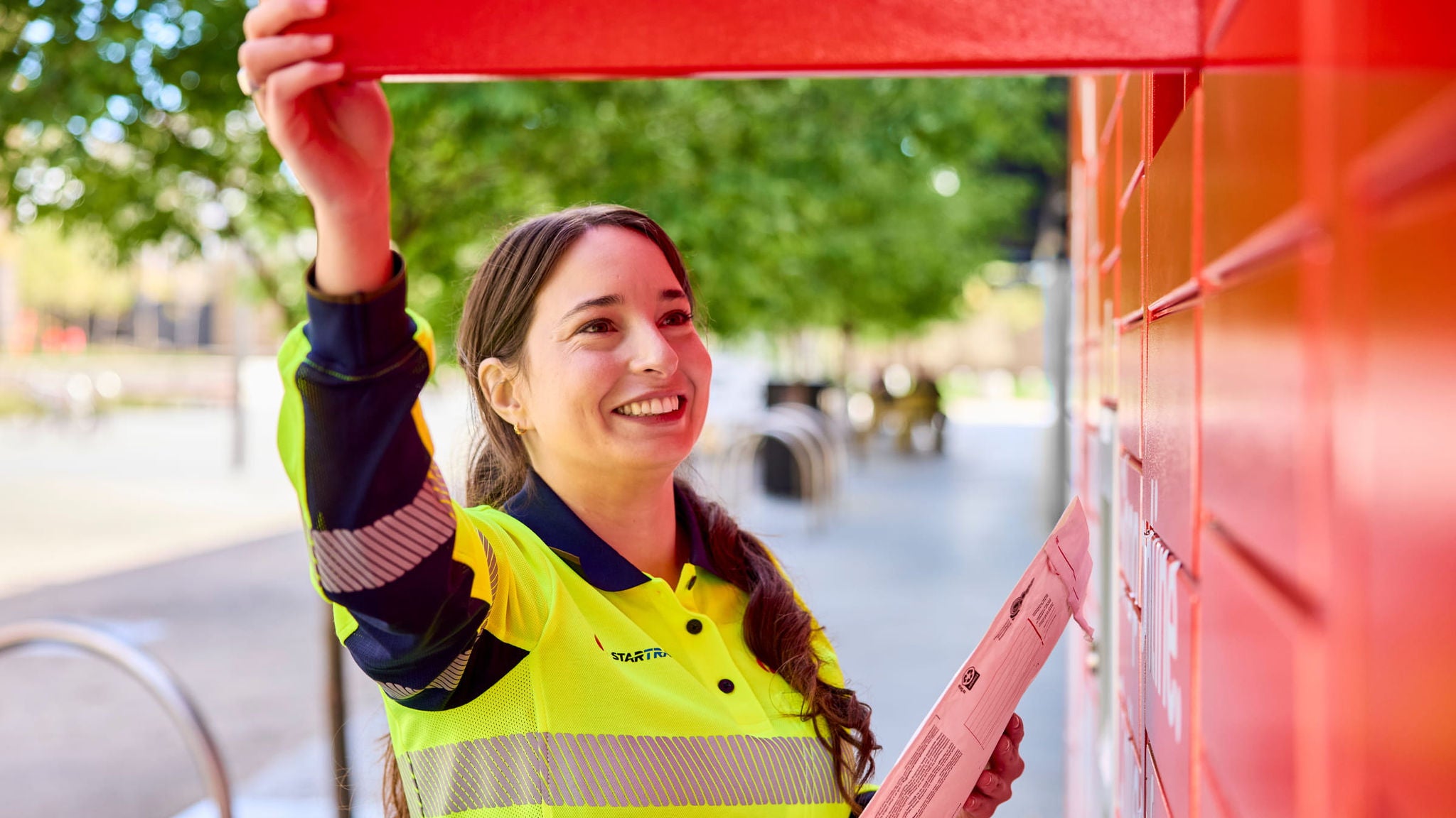 Female postie putting a parcel into a parcel locker