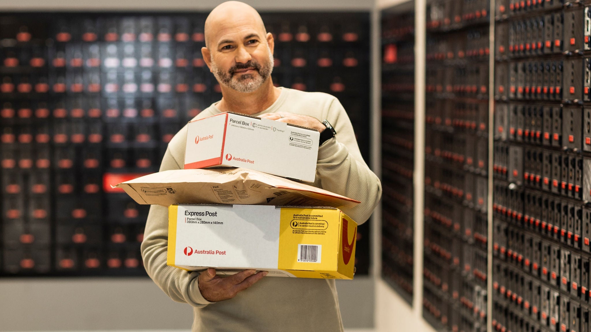photo-man-holding-box-and-parcels-walking-in-front-of-post-office-boxes