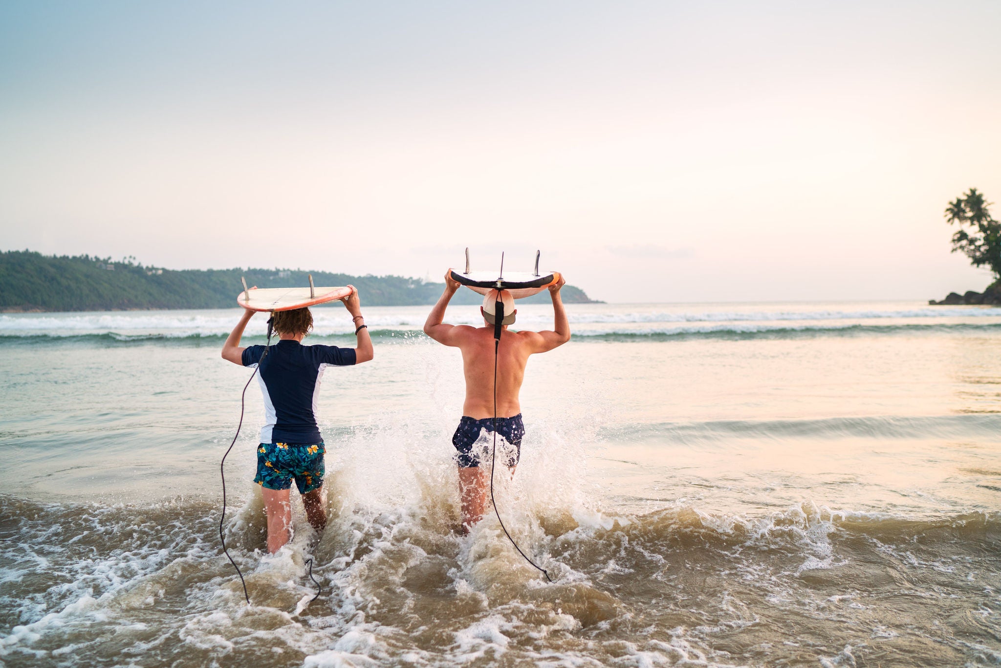 photo-two-people-walking-into-water-carrying-surboards